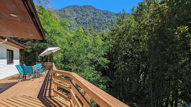 A wooden deck with outdoor furniture, a railing, and a view of a forested mountain. - Kari Mapu Park (Pucón)