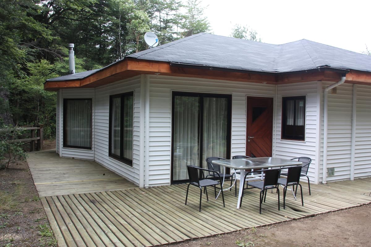 A single-story house with a deck, a dining table with chairs, and a satellite dish.