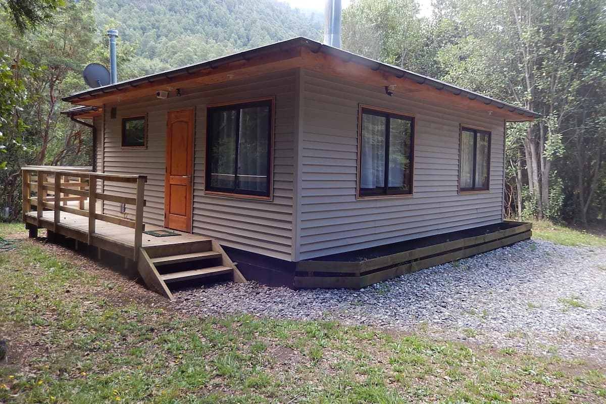 A small cabin with a wooden deck, a door, and two windows.