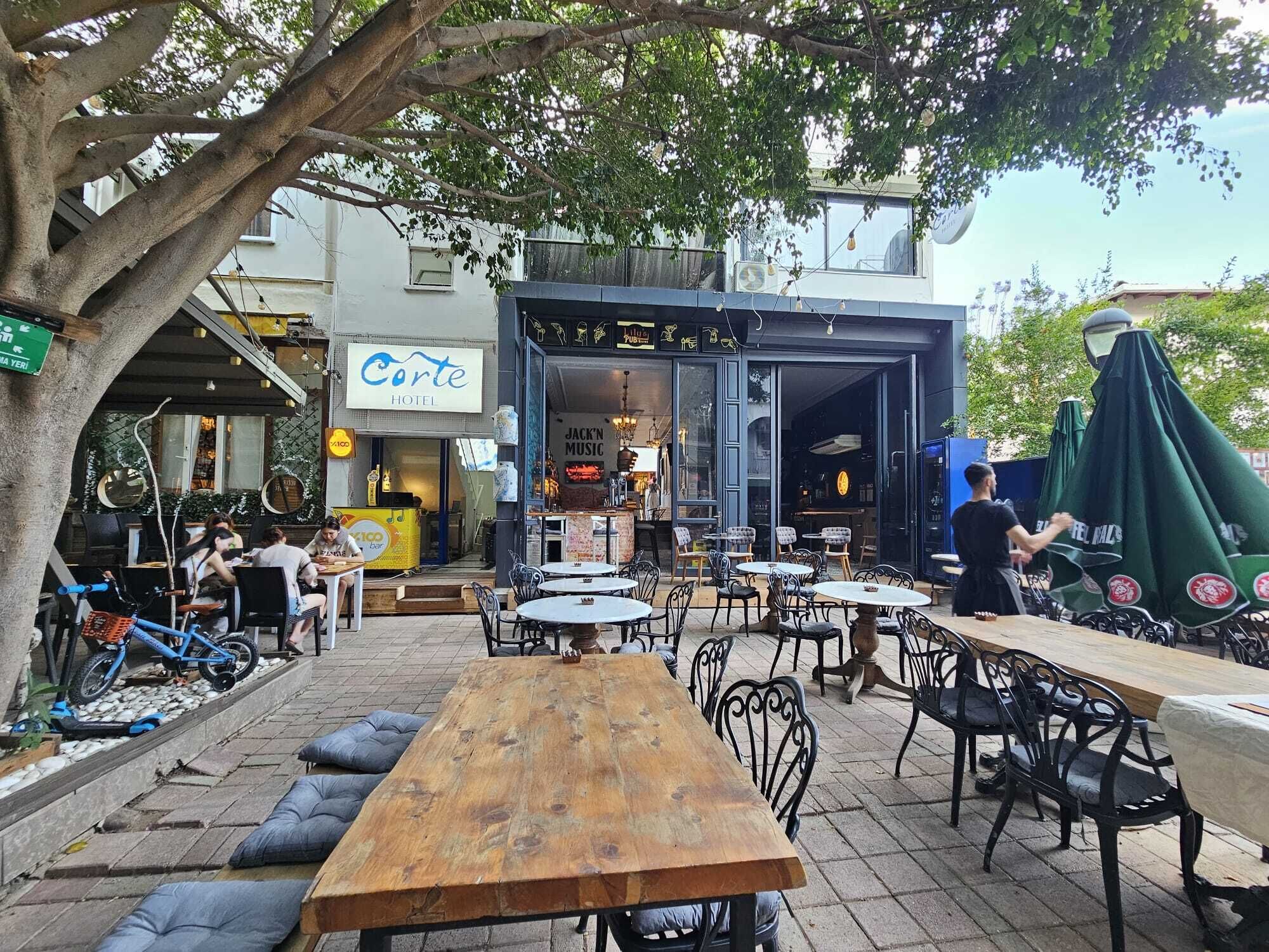An outdoor café with tables and chairs, a visible hotel sign, and a bar area.