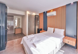 Una habitación de hotel moderna con una cama grande, un panel de pared de madera, un equipo de aire acondicionado y una mesita de noche pequeña.