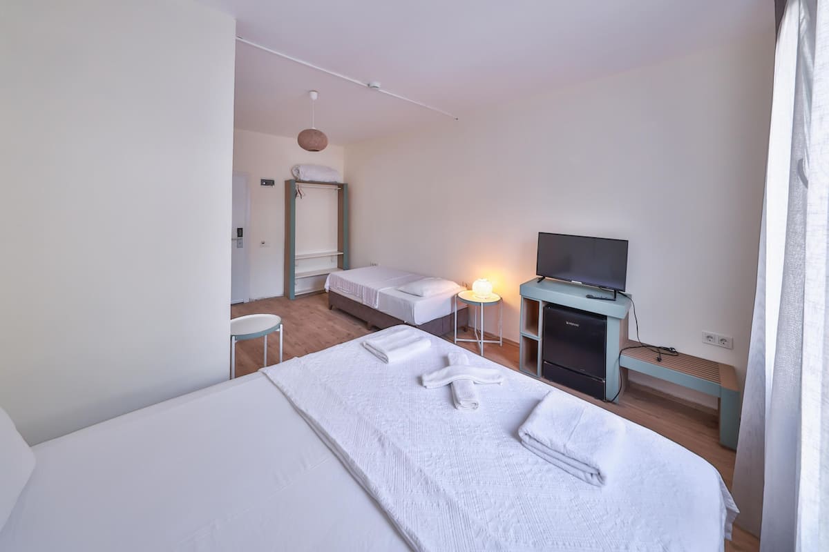 Hotellihuone, jossa on sänky, jalustalla oleva televisio, yöpöytä lampun kanssa ja pieni työpöytä.