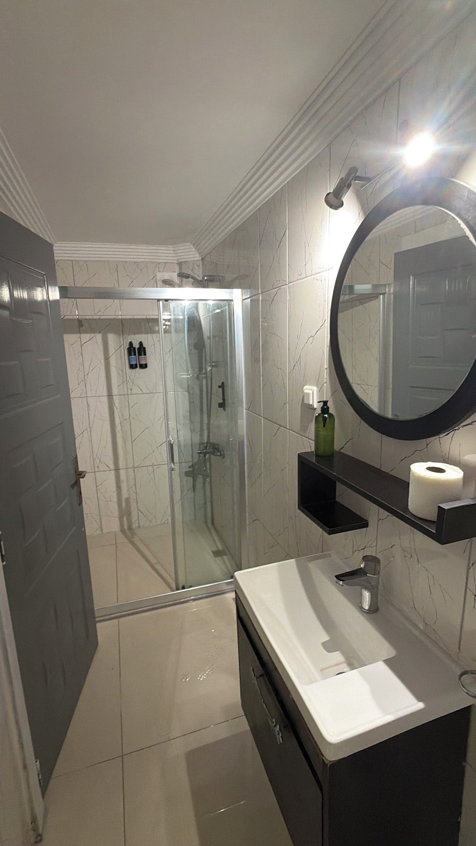 A bathroom with a glass shower enclosure, a white sink, a mirror, and a toilet paper holder.