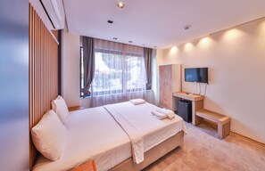 A modern hotel room with a large bed, a TV, a small desk, and a window with curtains. - Corte Hotel Kaş (Kas)