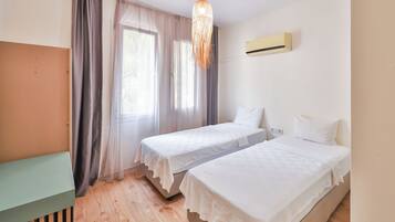 A room with two beds, a desk, a hanging light fixture, and an air conditioning unit.