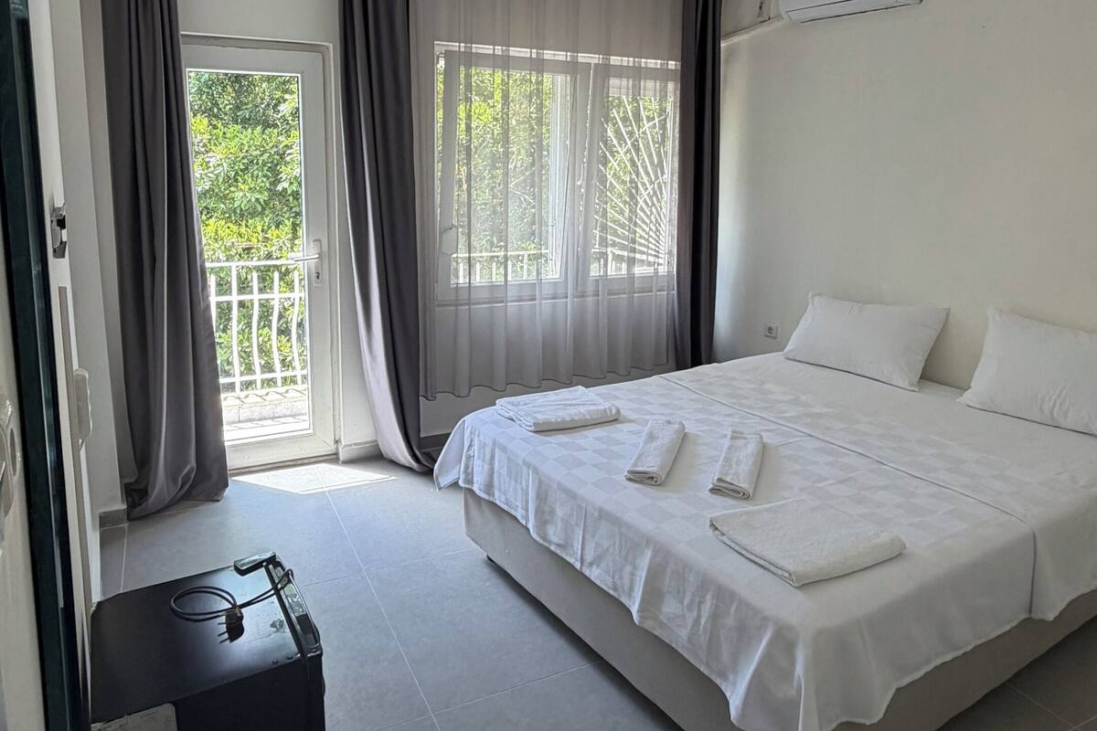 Hotellihuone, jossa on sänky, matkalaukku, ikkuna verhoilla ja ilmastointilaite.