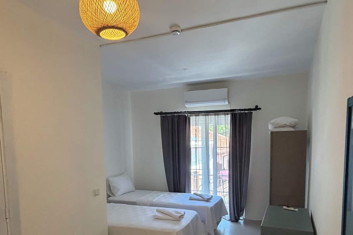 Ett hotellrum med två sängar, ett litet bord, en hängande lampa och en luftkonditioneringsanläggning.