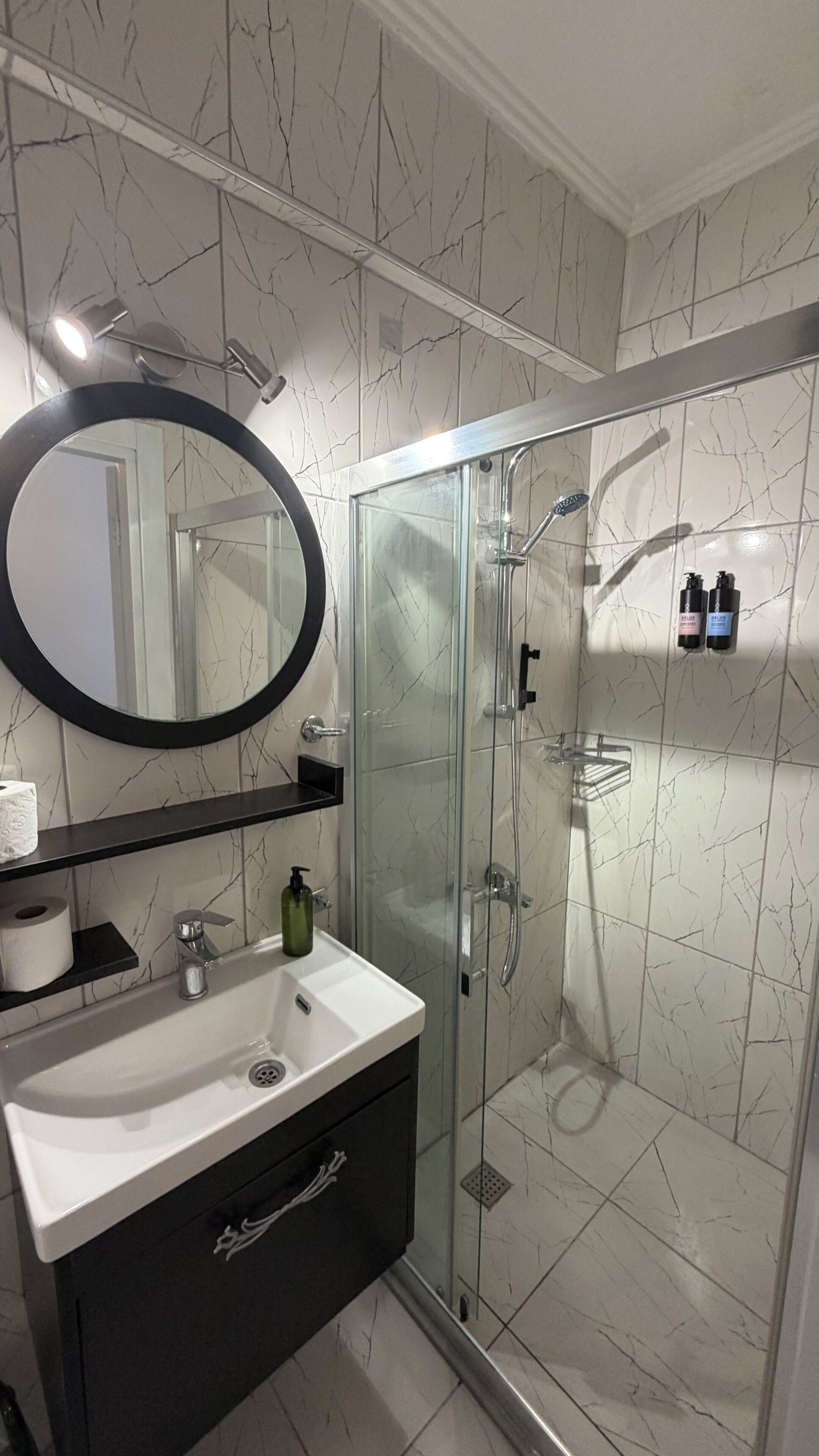 Un baño moderno con ducha de mampara de vidrio, un espejo redondo y un lavabo blanco.