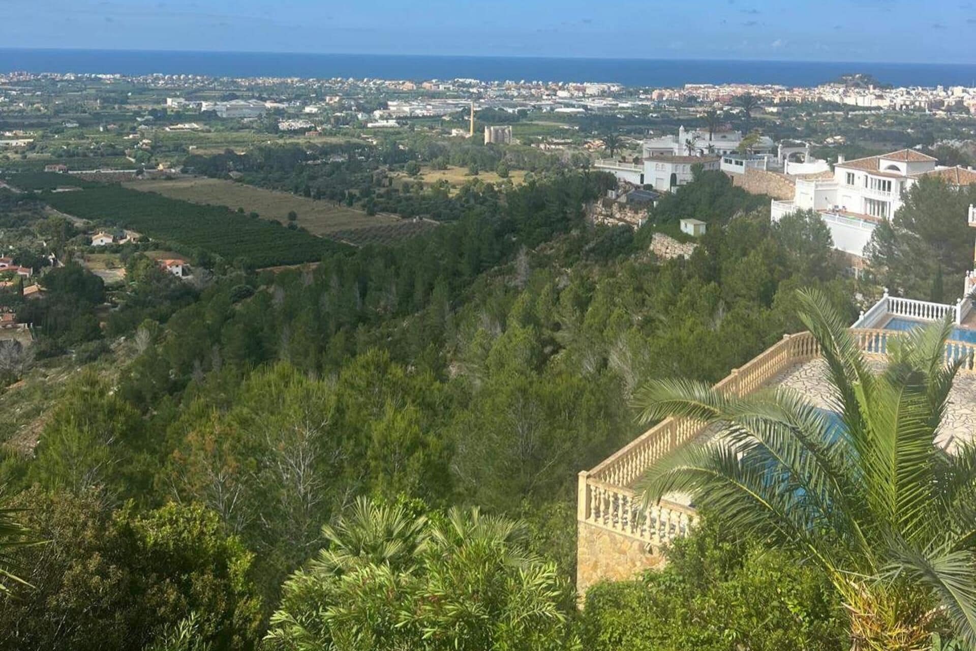 A coastal town with dense greenery, a prominent white building with a balcony, and a view of the sea.