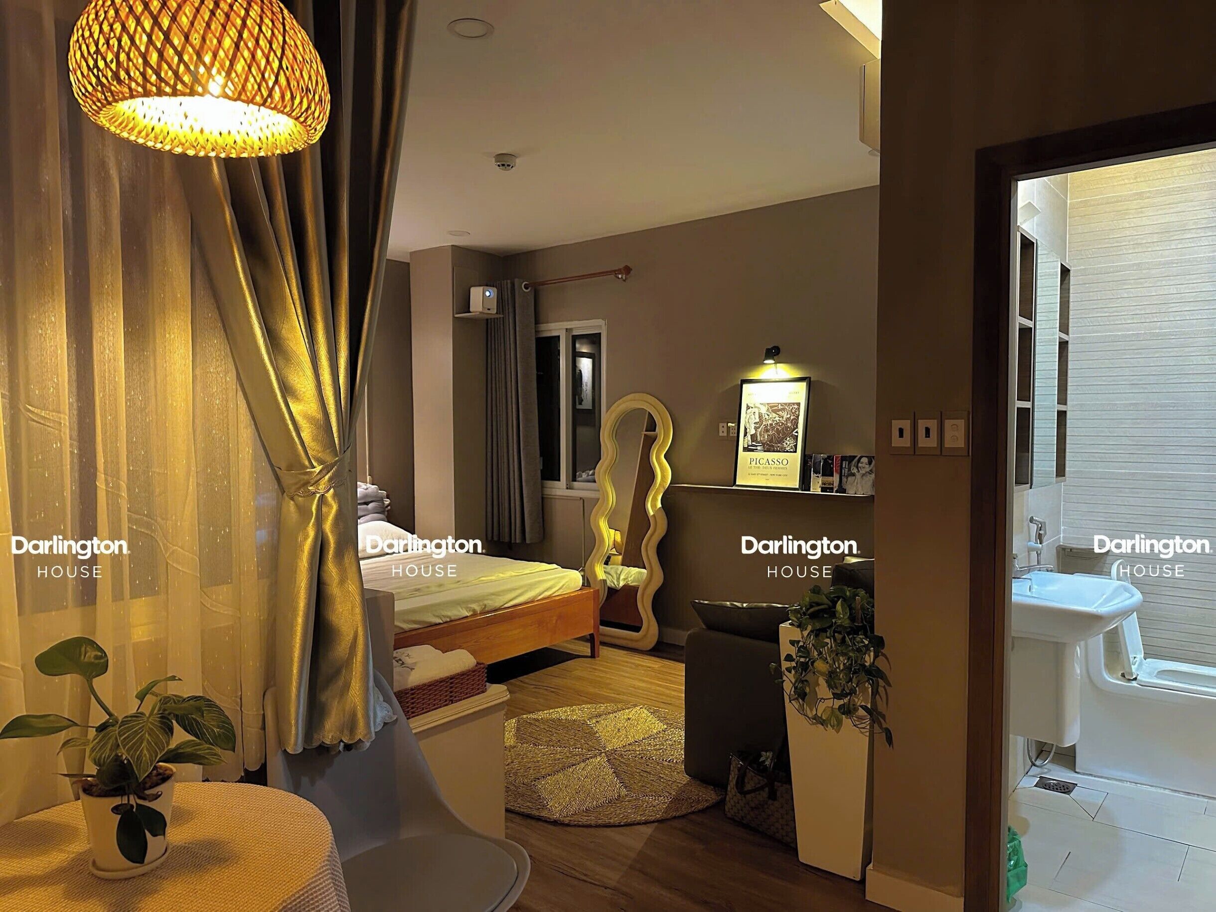 Une chambre d’hôtel avec un lit, une table de chevet ornée d’une plante, un miroir et une fenêtre avec des rideaux.