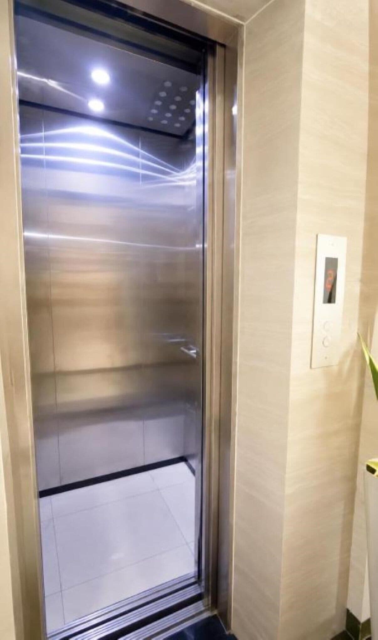 An elevator with a metallic interior, a control panel on the wall, and a tiled floor.