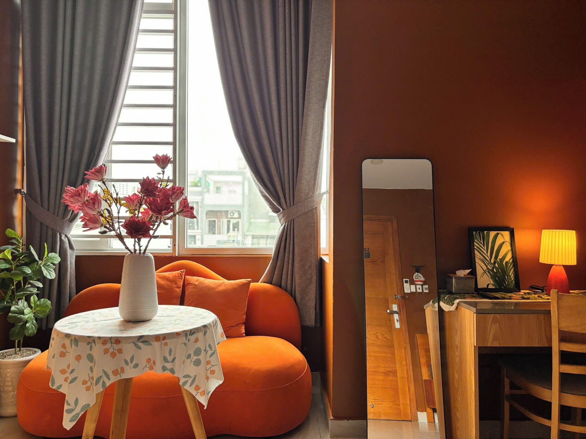 Une pièce avec une table ronde, des sièges orange, une plante en pot, un miroir et une lampe.