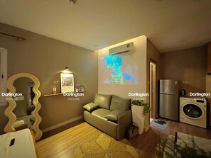 En moderne stue med sofa, sofabord, vægmonteret projektor, vaskemaskine og et spejl.