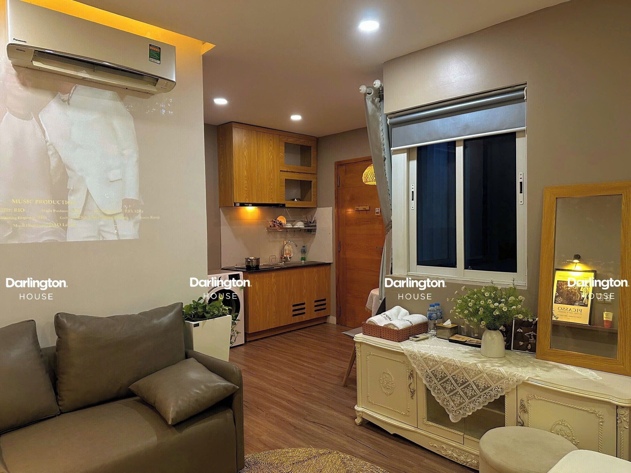Un espacio habitable compacto con kitchenette, un sofá, una mesa de comedor y una ventana con cortina.