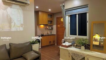 Un espacio habitable compacto con kitchenette, un sofá, una mesa de comedor y una ventana con cortina.