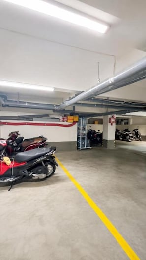 En parkeringsgarage med beton gulve, gule parkeringsmarker og flere motorcykler parkeret.