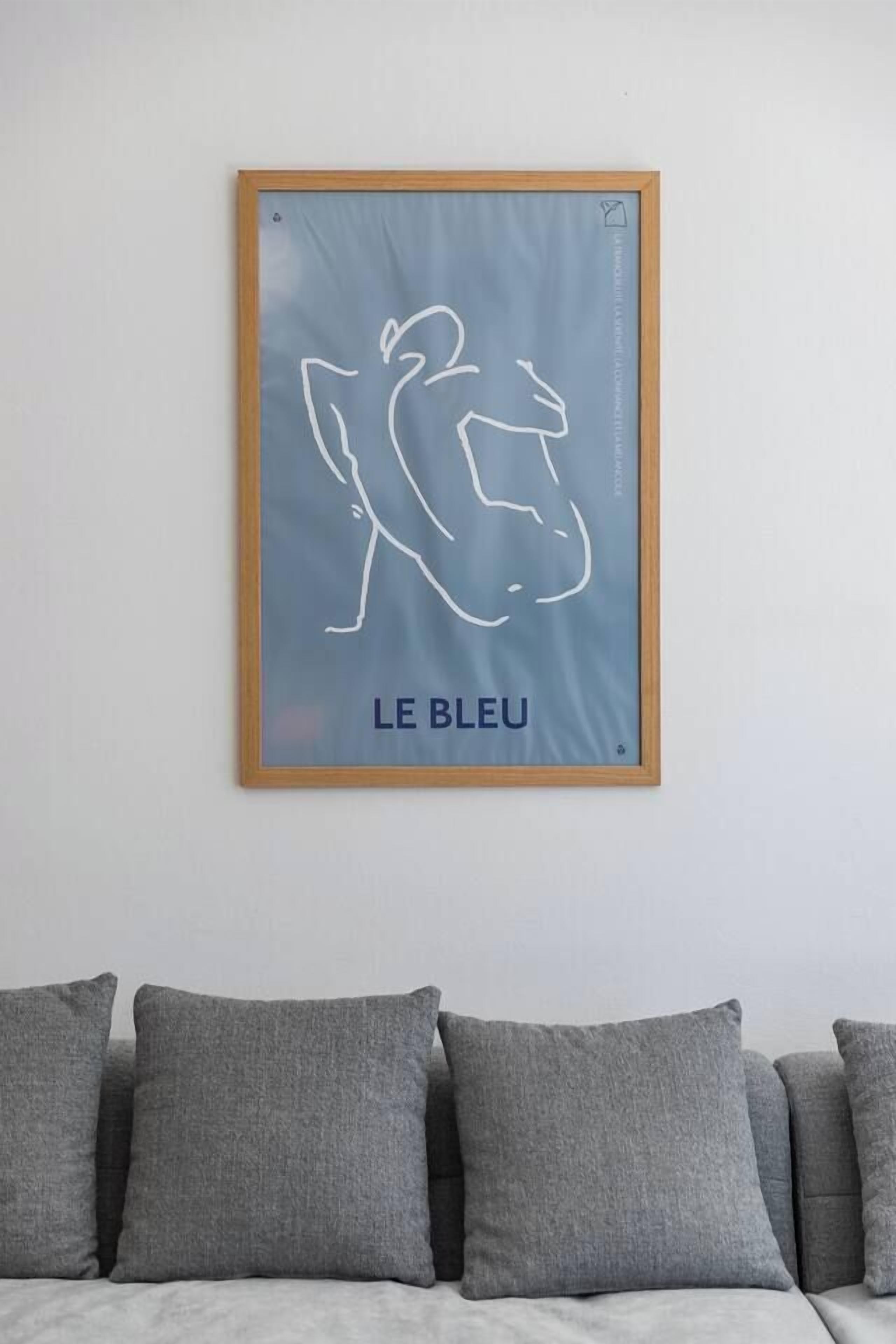 Un'opera d'arte incorniciata con un disegno a linea e il testo 'LE BLEU' appesa a una parete sopra un divano grigio.