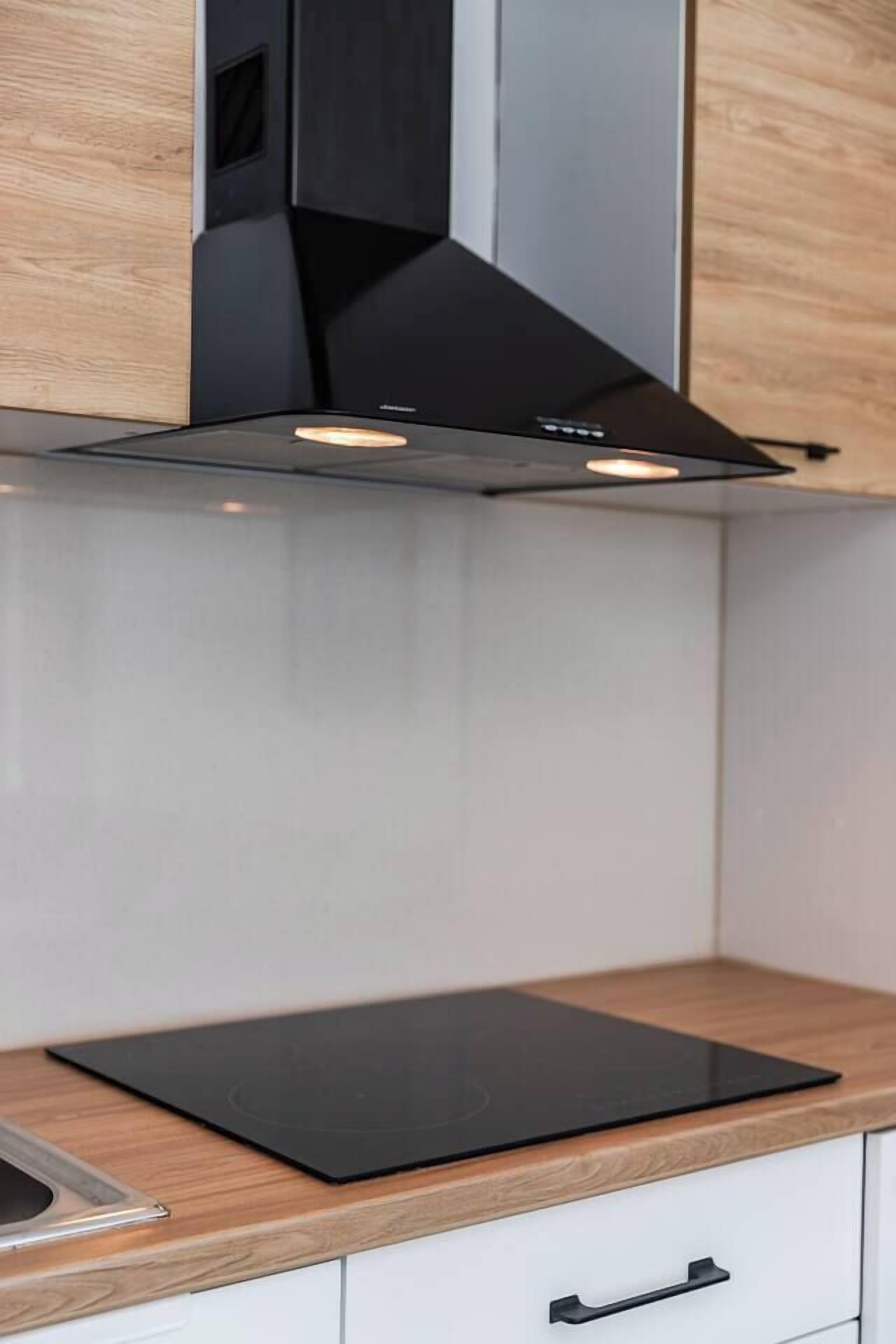 Una cocina con una campana extractora negra, una encimera de madera y un armario blanco.