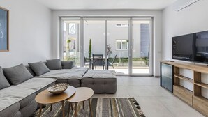 Un salon moderne avec un canapé d’angle, un téléviseur et une porte-fenêtre coulissante donnant sur un espace extérieur.