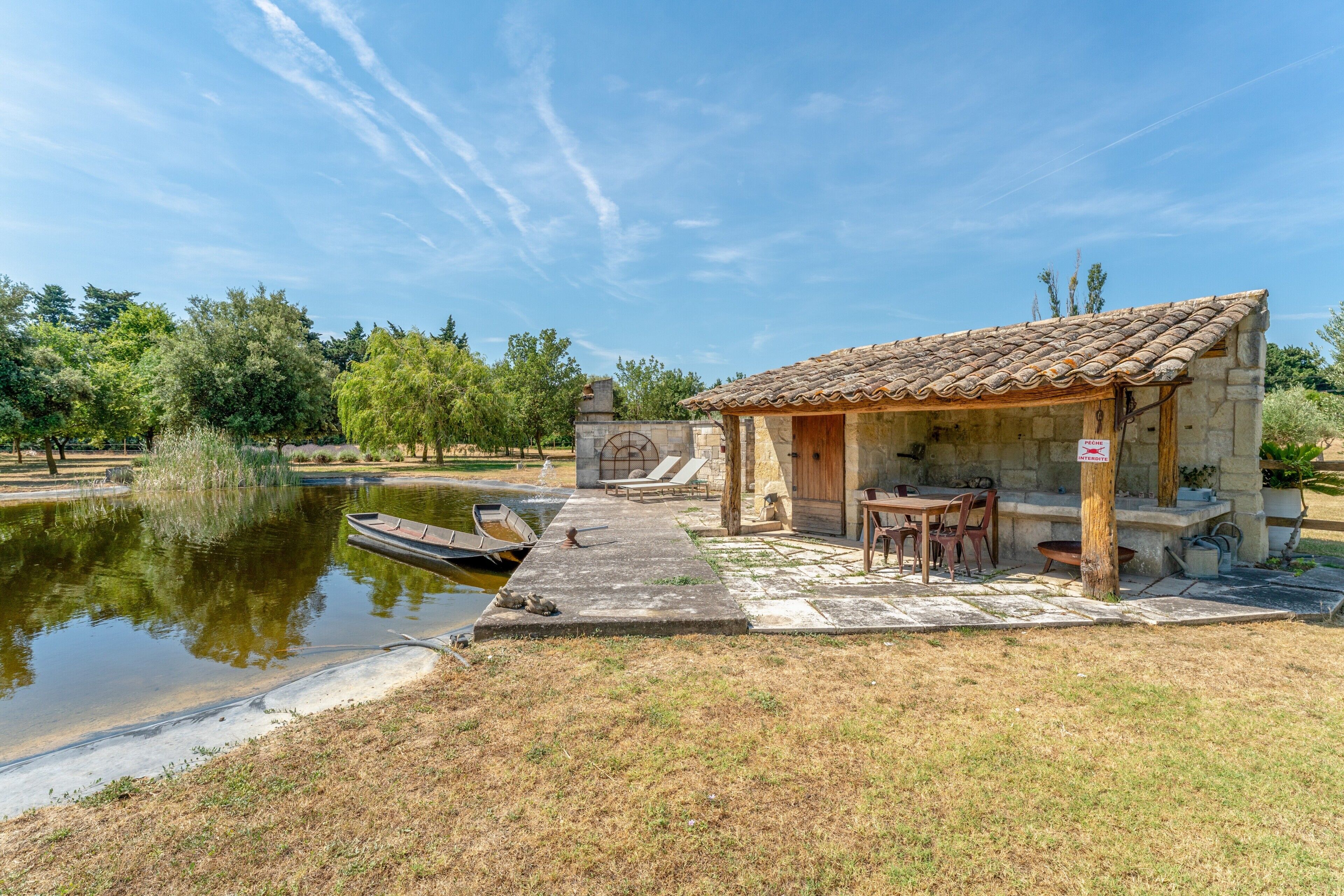 Un petit bâtiment en pierre avec un toit en tuiles, un étang et un bateau amarré au bord de l’eau.