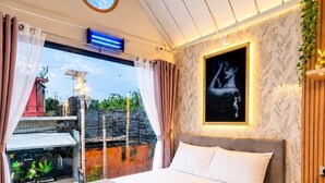 A modern hotel room with a large bed, a view of the outside, a ceiling light, and a wall-mounted artwork. - Near BKK Homestay Airport (Bang Phli)