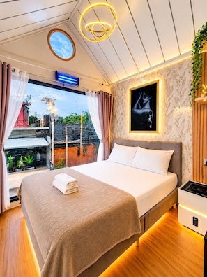 Ein modernes Hotelzimmer mit einem großen Bett, Blick ins Freie, einer Deckenleuchte und einem an der Wand befestigten Kunstwerk.