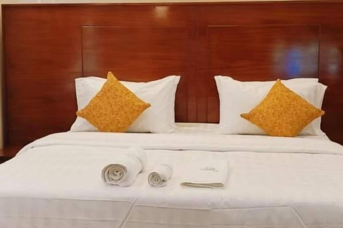 Una habitación de hotel con cabecera de madera, ropa de cama blanca y paneles decorativos en el techo.