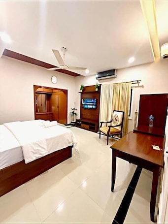 A hotel room with a bed, a desk, a chair, a television, and an air conditioning unit.