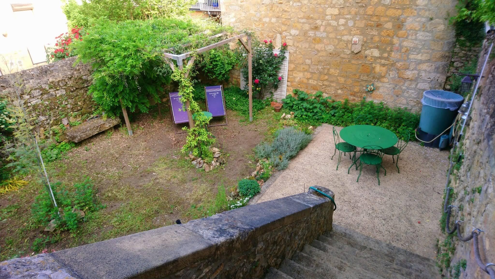 A stone wall, a garden with plants and a table with chairs, and a purple object.