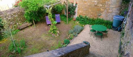 A stone wall, a garden with plants and a table with chairs, and a purple object.