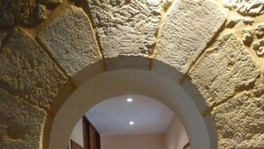 A stone archway leading to a bedroom with a bed and a nightstand. - The chaplain's dwelling (DOMME)