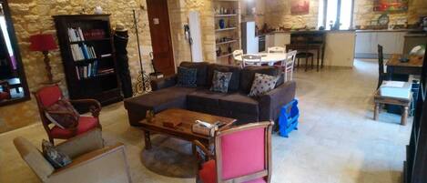 A living room with a sofa, a coffee table, a bookshelf, and a dining area with chairs and a table.