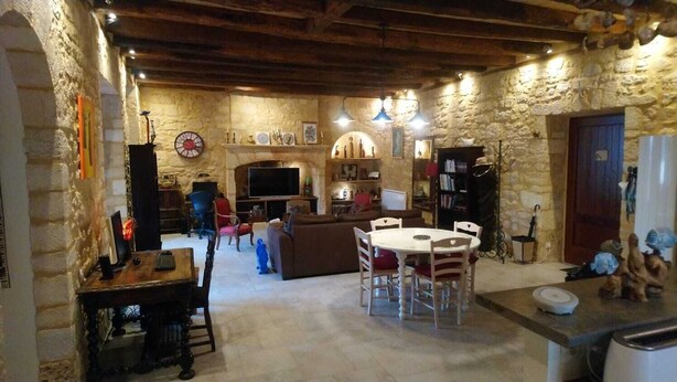 A rustic stone interior with a fireplace, wooden beams, a dining area, and a television. - The chaplain's dwelling (DOMME)