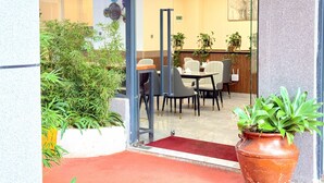 Entrada de hotel con puerta de cristal, zona de estar interior y plantas en macetas.