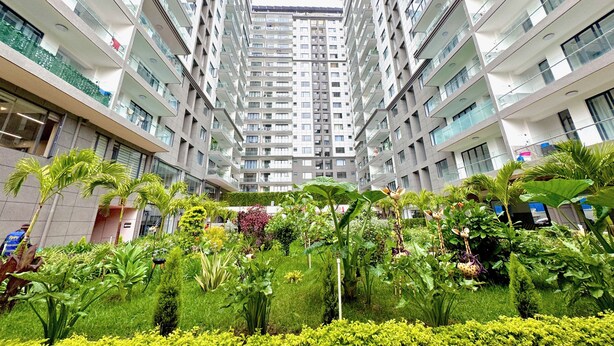 Un moderno edificio de apartamentos con varios pisos, balcones y un jardín bien cuidado con diversas plantas.