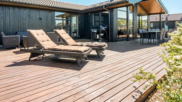 Una casa moderna con una terrazza in legno, poltrone relax e zona pranzo.