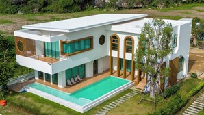 Ett modernt hus i två våningar med en swimmingpool, stora fönster och en välskött gräsmatta.