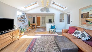 A spacious living area with a large flat-screen TV, wooden furniture, a patterned rug, and a high ceiling with skylights.