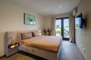 Ein modernes Schlafzimmer mit einem großen Bett, einem Nachttisch, einem an der Wand montierten Fernseher und Blick ins Freie.