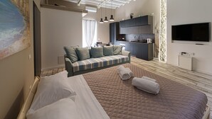 Ein modernes Hotelzimmer mit einem großen Bett, einer Sitzecke, einer Küchenzeile und einem an der Wand befestigten Fernseher.