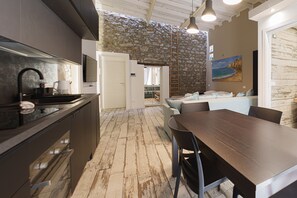 Eine moderne Küche mit Steinwand, ein Essbereich mit Holztisch und -stühlen sowie ein Wohnbereich mit Sofa und einem Gemälde.