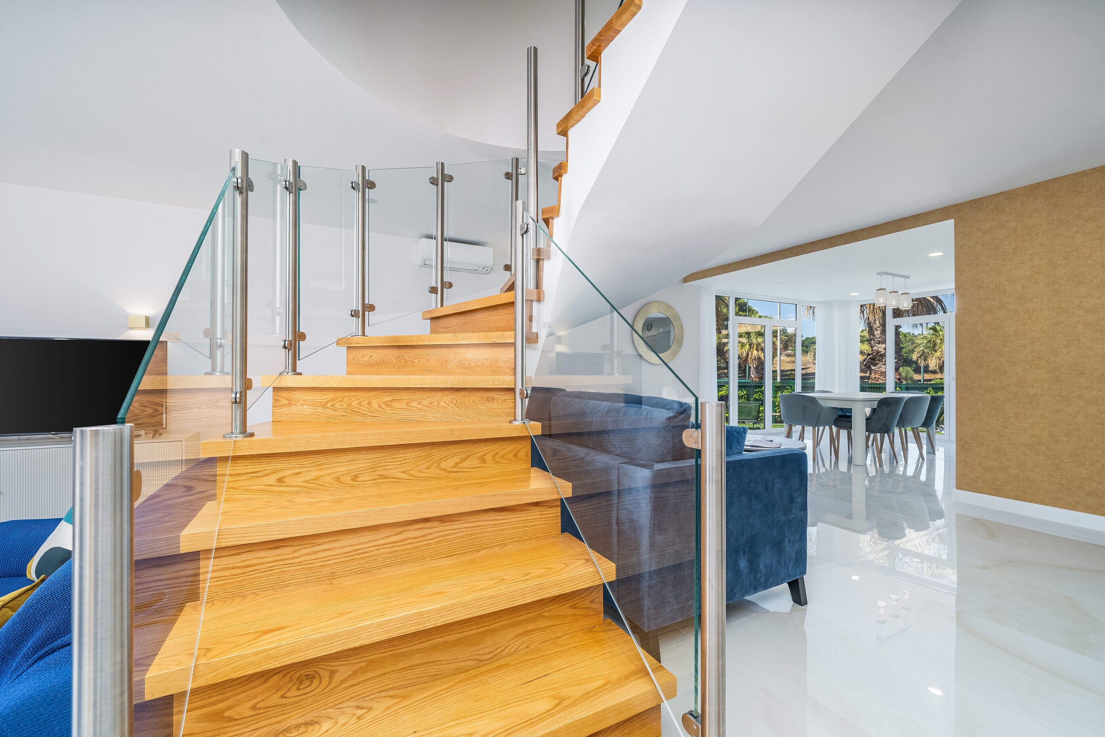 A modern staircase with glass railings and wooden steps, leading to a dining area with a glass wall and outdoor view.
