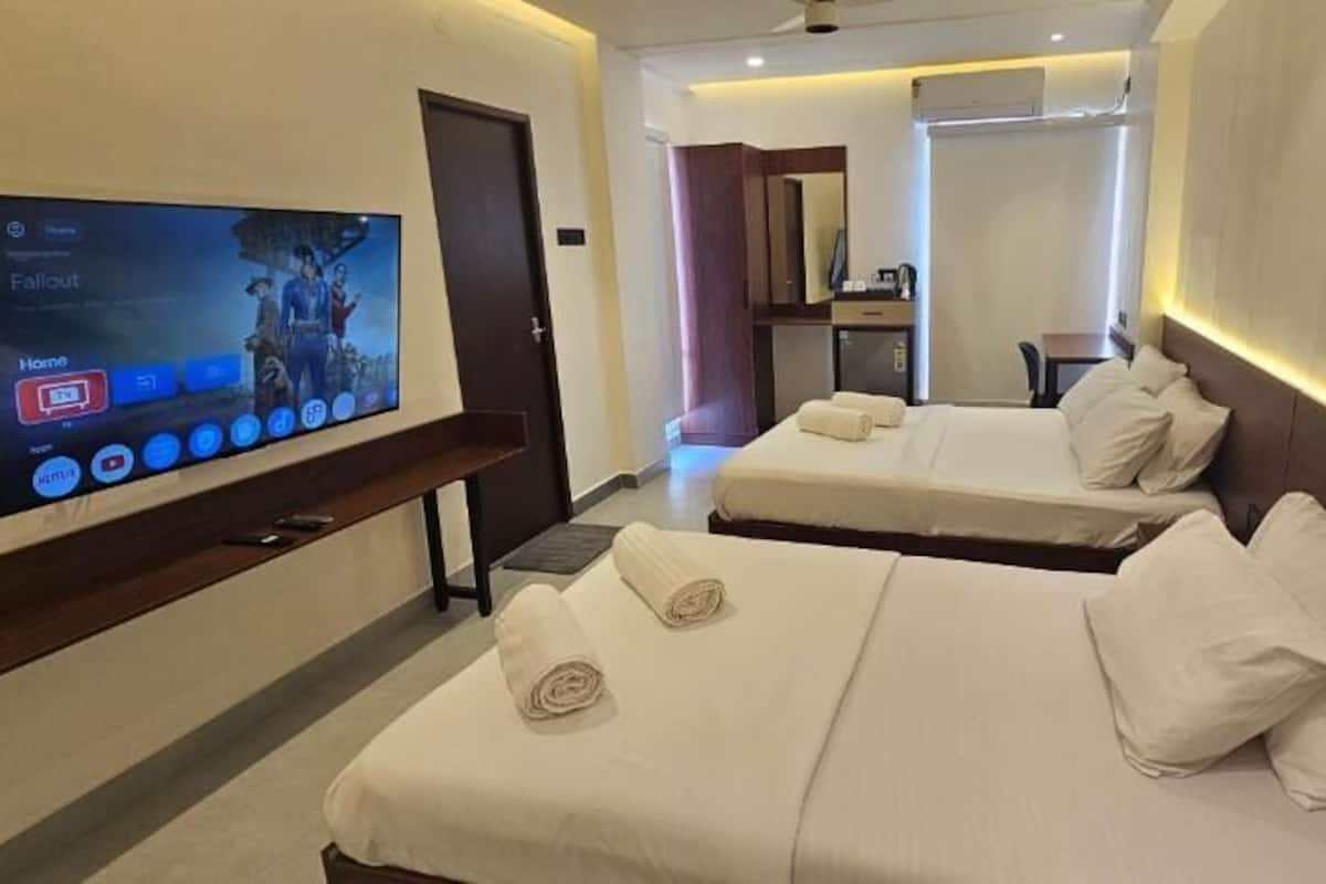 Habitación de hotel con dos camas, un televisor mostrando un partido, un escritorio y un espejo.