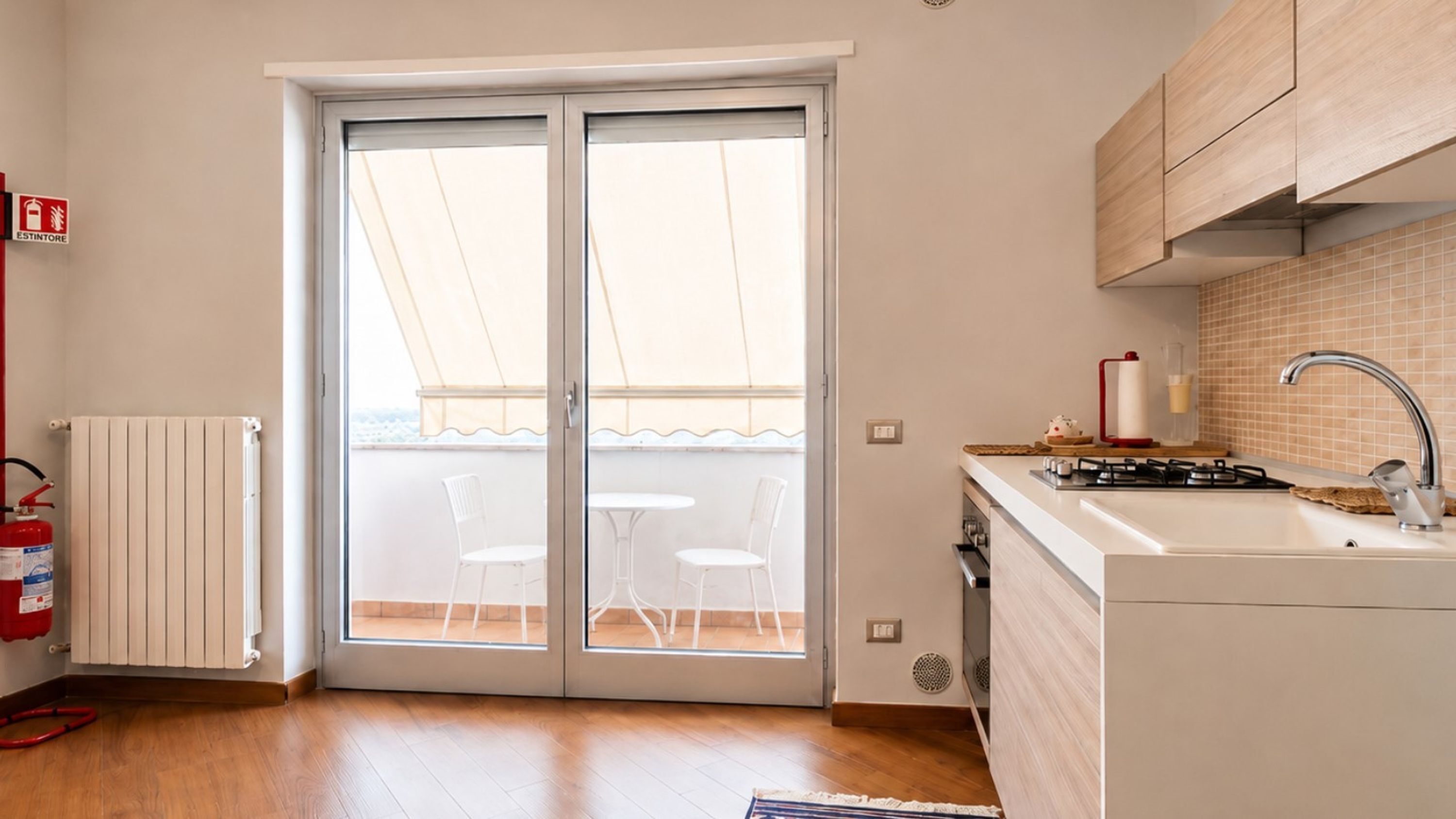 Una cucina con piano cottura integrato, lavello e una porta vetrata scorrevole che dà su un balcone.