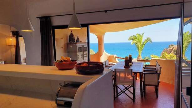 Ein modernes Zimmer mit Meerblick, einer Essecke mit Tisch und Stühlen sowie einer Küchenzeile mit Obstschale.