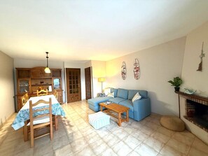 A living room with a blue sofa, wooden dining table, and chairs, a small coffee table, and a fireplace. - Casa Cala Bot - Private Mediterranean escape in Costa Dorada (Miami Platja)