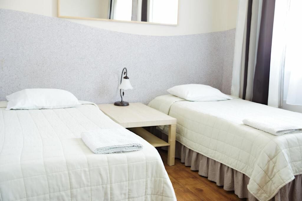 A hotel room with two beds, a nightstand, a lamp, and a window with curtains.