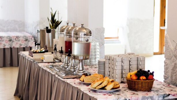 A breakfast buffet setup with a long table, beverage dispensers, and a fruit basket. - Hotel Nevada (Lagow)