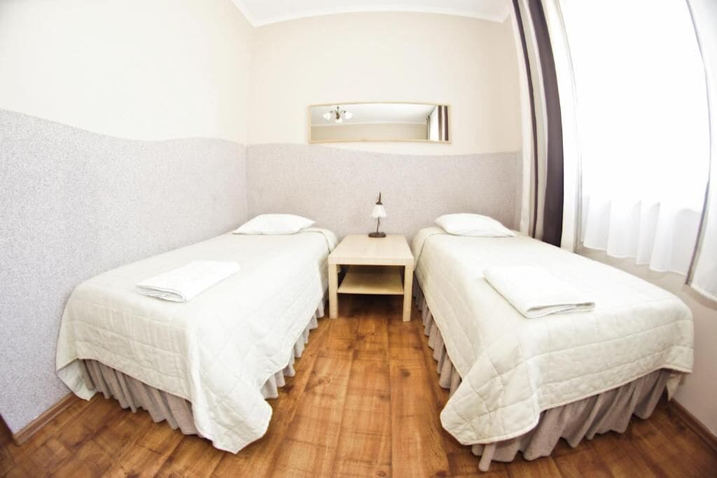 Une chambre avec deux lits, une petite table, un miroir et une fenêtre avec des rideaux.