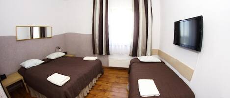 A hotel room with two beds, a TV, a window with curtains, and a mirror.